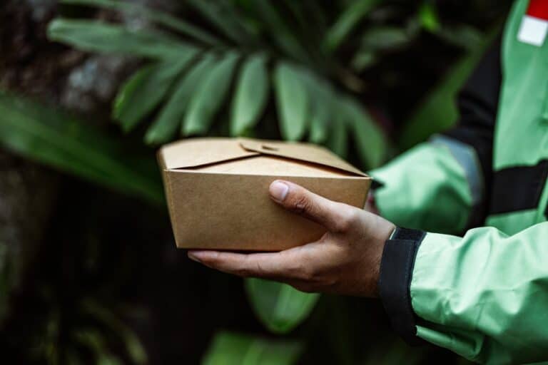 Kurier trzyma kartonowe opakowanie na tle zieleni — opakowania wielokrotnego użytku w e-commerce