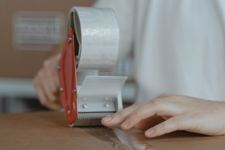 Zaklejanie kartonu taśmą pakową przy użyciu podajnika na stanowisku pakowania